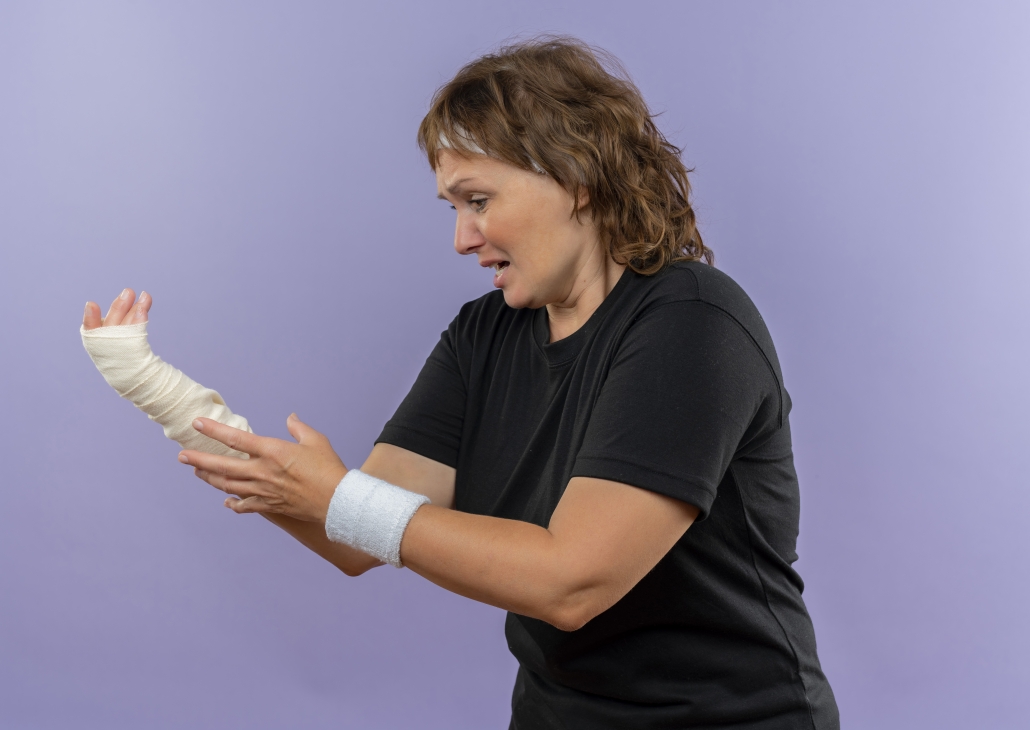 upset middle aged sporty woman in black t-shirt with headband holding her bandaged wrist having pain standing over blue background #injuryprevention, #physicaltherapy, #fitness, #rehab, #physiotherapy, #injury, #mobility, #physio, #health, #injuryrecovery, #rehabilitation, #recovery, #strengthandconditioning ,#sportsmedicine ,#backpain, #prehab, #sportsinjury, #exercise, #strengthtraining, #wellness, #painrelief, #strength ,#training, #physicaltherapist ,#sportsperformance, #workout, #sportstherapy ,#movement, #sportsrehab, #injuryrehab
